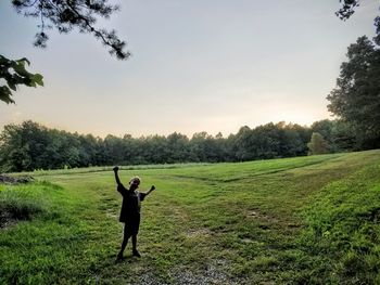 Full length portrait of boy arms outstretched standing on grassy field against clear sky