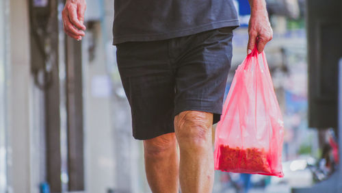 Midsection of man holding plastic bag while walking in city