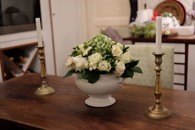 Close-up of fresh white roses in vase amidst candlestick holders on table