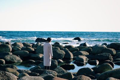 Rear view of woman standing at beach on sunny day