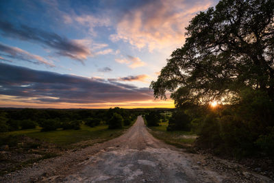 Road amidst trees against sky during sunset