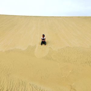 Low angle view of man sitting on sand dune against clear sky