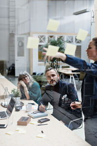 Female professional explaining adhesive notes to coworkers at office