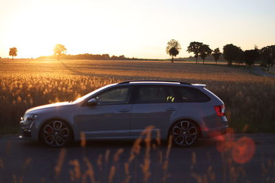 Car on road by field against sky during sunset