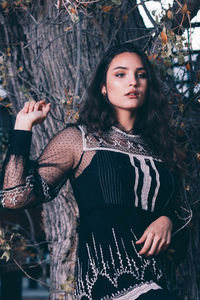 Portrait of young woman standing against tree