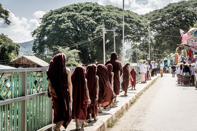 Rear view of monks walking on footpath by road at city during sunny day