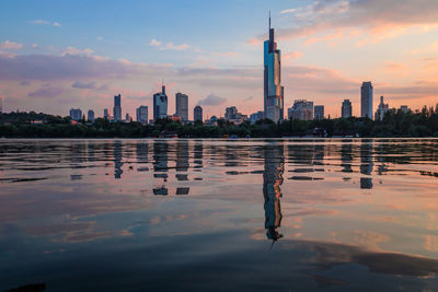 Reflection of buildings in city against sky during sunset