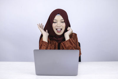 Portrait of young woman using mobile phone against wall