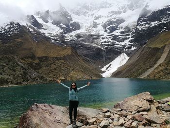 Woman with arms outstretched standing against lake and mountains