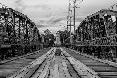 Rear view of woman practicing headstand on wooden footbridge against sky