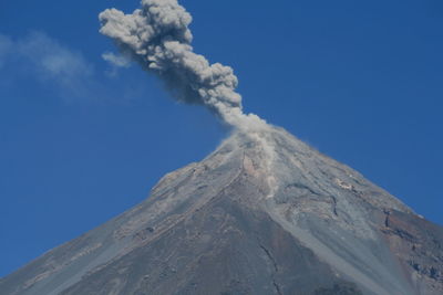 Low angle view of volcanic mountain against blue sky