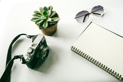 High angle view of camera with book and sunglasses on white background