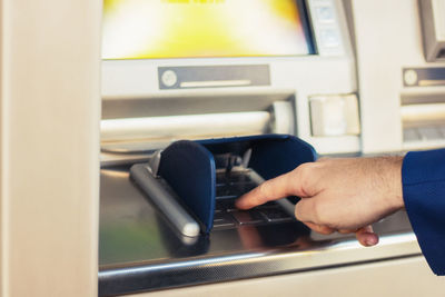 Cropped hand of man using atm machine