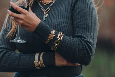 Midsection of woman in warm clothing wearing bracelet holding wineglass outdoors