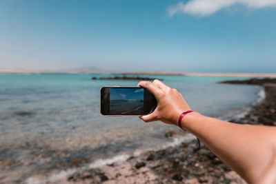 Man photographing sea through smart phone on beach