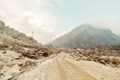 Dirt road by mountains against sky