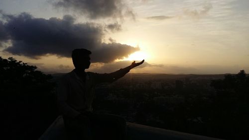 Silhouette man standing on city against sky during sunset