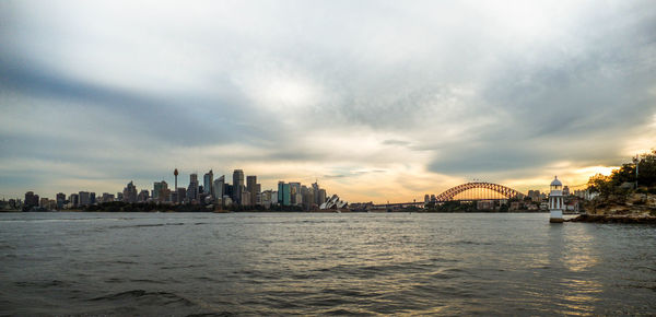 View of city at waterfront against cloudy sky