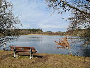 Empty bench by lake against sky