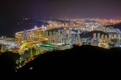 Illuminated city by river against sky at night