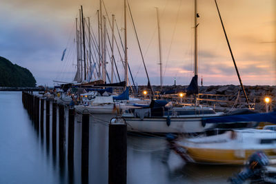 Sailboats moored in harbor at sunset