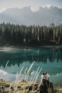 Rear view of men sitting by lake against mountain