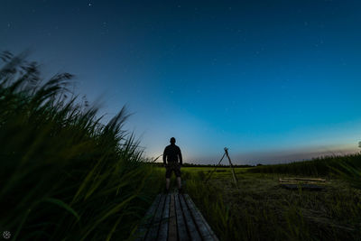 Rear view of man standing on field against sky at night