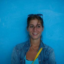 Smiling young woman looking away while standing against blue wall