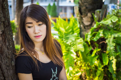 Portrait of beautiful young woman against tree trunk