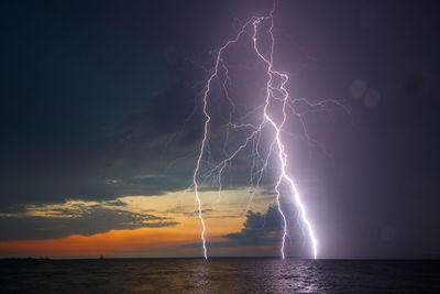 Forked lightning over sea against sky during sunset