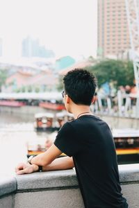 Rear view of man sitting on retaining wall against city