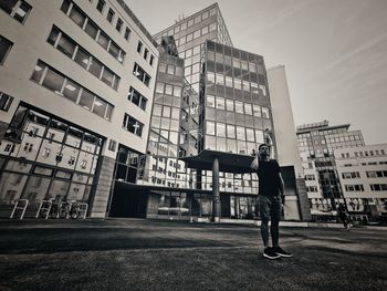Rear view of man standing by buildings in city against sky