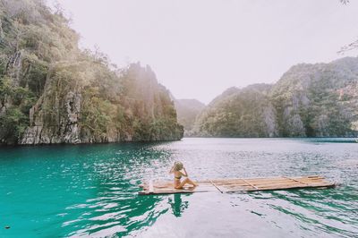 Side view of woman sitting on wooden raft in kayangan lake against sky