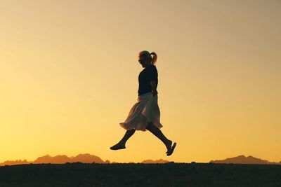 Side view of woman jumping against clear sky during sunset