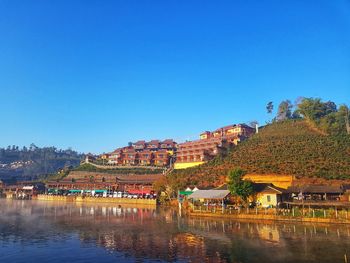 Buildings by river against clear blue sky