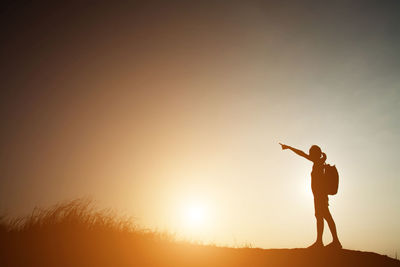 Silhouette hiker pointing while standing on field against sky during sunset