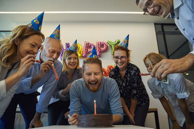 Colleagues having a birthday celebration in office with cake, party blower and party hats