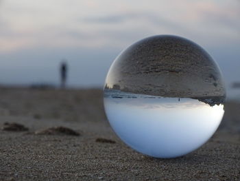 Close-up of crystal ball on beach against sky