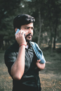 Young man talking on phone while standing against trees