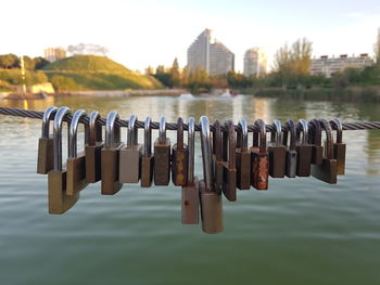 Padlocks hanging on metal by river against sky