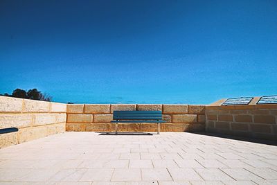 Empty bench by swimming pool against clear blue sky