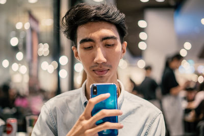 Close-up of man using mobile phone in illuminated store