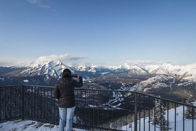 Rear view of man standing on snowcapped mountain against sky