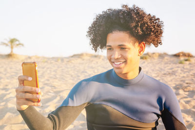 Young african american man sitting on the sand takes a picture with a smartphone