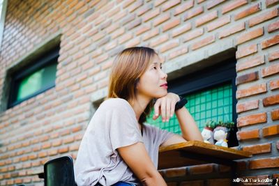 Young woman looking away against brick wall