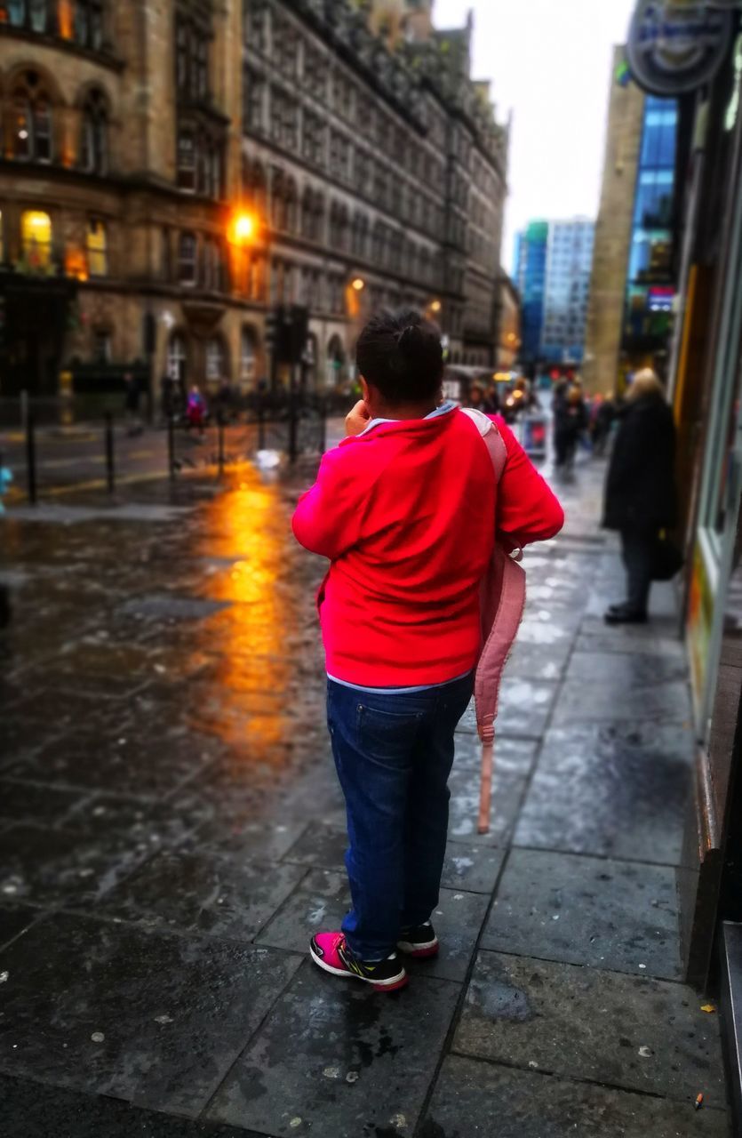 REAR VIEW OF MAN WALKING ON STREET IN CITY