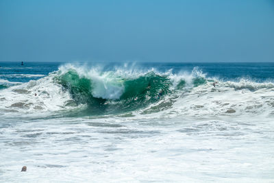 Waves splashing on shore against clear sky