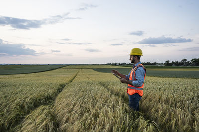 Engineer in reflective clothing holding tablet pc amidst crop in field
