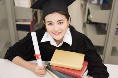 Smiling young woman in graduation gown holding diploma