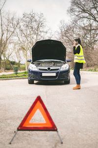 Young  woman talking on her cell phone while her car is broken down on the road.